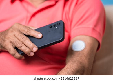 Close up shot of senior man checking sugar or glucose level by tapping mobile phone to sensor at home - concept of technology, diabetes and health care - Shutterstock ID 2314623369
