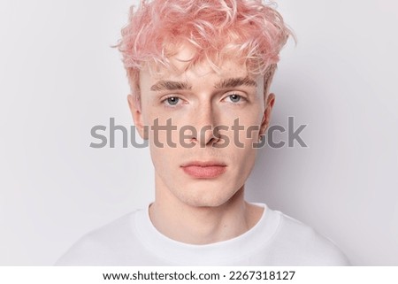 Close up shot of serious attentive pink haired man with earring dressed casually has calm expression looks directly at camera isolated over white background has unusual appearance. Youth concept