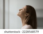 Close up shot side profile face view of beautiful young 30s blissful woman enjoy pleasant fragrance, breathing fresh conditioned air inside room, closing her eyes dreaming feeling happy and peaceful