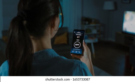 Close Up Shot Of A Smartphone With Active Smart Home Application. Young Woman Is Tapping The Screen To Turn On The Light In The Room. It's Cozy Evening In The Apartment.