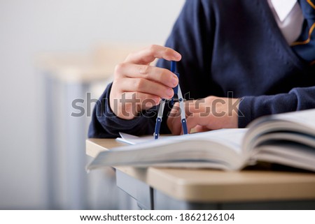 A close up shot of a student's hand using a drawing compass on a desk.