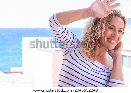 Close up shot of stylish curly woman smiling against blue sea background. Beautiful female model with copy space