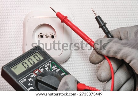 Close up shot technician in protective work gloves using red and black probes to test European electrical socket. Image represents home electrical safety, maintenance, and wiring inspection.
