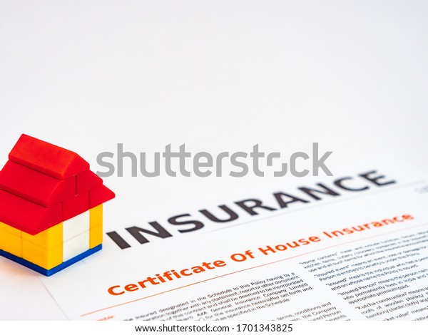 Close up shot of a toy house with insurance form below\
on white 