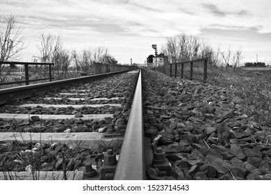 A close shot of train tracks in rocks near leafless trees under a cloudy sky in black and white - Powered by Shutterstock