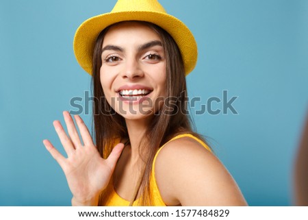 Close up shot traveler tourist woman in yellow summer casual clothes hat doing selfie on mobile phone posing isolated on blue wall background studio portrait. People lifestyle concept. Looking camera