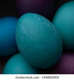 Close Up Shot Of A Turquoise Colored Easter Egg In A Bow Of Blue, Turquoise, And Purple Easter Eggs With Strong Shadows And Dark Background.