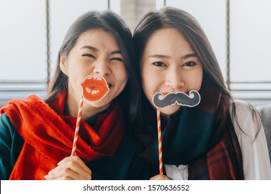 Close Up Shot Of Two Asian Women Friends Wearing Scarf Playing With Paper Props Having Fun Together