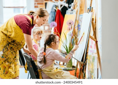 Close up shot of two Caucasian girls with Down's syndrome and their female teacher painting in art class at school. Concept of learning kids with disability. - Powered by Shutterstock