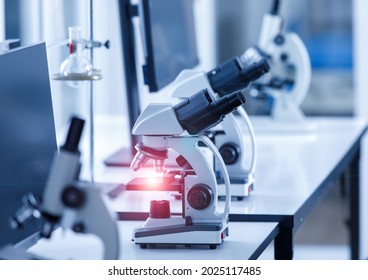 Close Up Shot Of Two Eyes Viewfinder Scientific Microscope Instrument With Red Light Flare At Lens And Glass Plate Sample In Row On Laboratory Working Desk Using For Monitoring Coronavirus Covid 19.