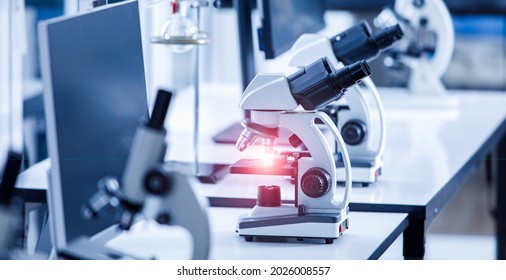 Close Up Shot Of Two Eyes Viewfinder Scientific Microscope Instrument With Red Light Flare At Lens And Glass Plate Sample In Row On Laboratory Working Desk Using For Monitoring Coronavirus Covid 19.