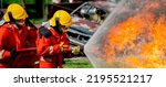 Close up shot two firefighters support to douse or quell fire using sprinkler and fire be controlled inside water curtain. The firefighters work near crashed car with day light.