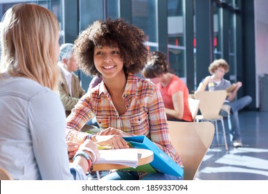 Eine Nahaufnahme von zwei jungen Mädchen, die in der Schule miteinander sprechen, mit dem Lehrer den Schülern im Hintergrund hilft.