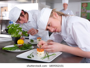 A close up shot of two young trainee chefs garnishing desert in a kitchen.