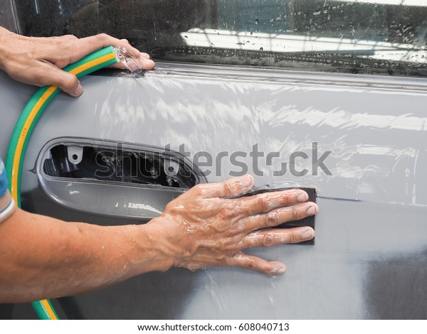 Close up shot of unidentified Asian worker\'s hand\
scrubbing water sandpaper on the door of the car to get ready for\
paint job