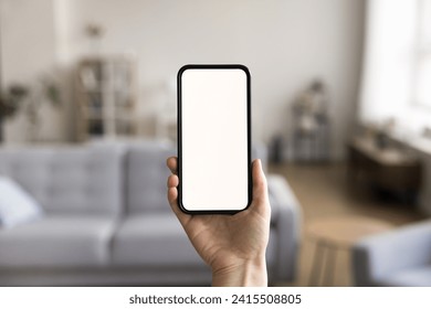 Close up shot of unknown female hand holding modern smartphone with white mock up blank screen, living room on background. Advertisement of new mobile application ad, smart home app, comfort living