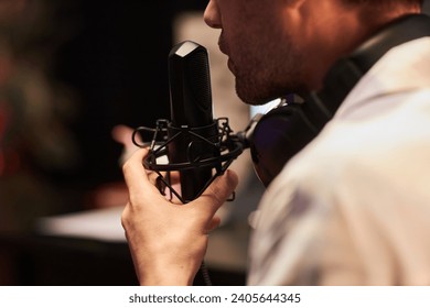 Close up shot of unrecognizable man with headphones on neck using professional microphone in studio