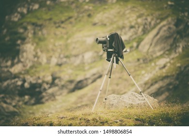 Close up shot of a vintage camera on a tripod, backed by a mountain.