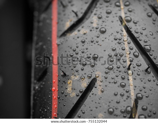 Close up shot of water drops on brand new\
motorcycle tire with red and yellow stripes mark on the surface.\
Close up shot shows the thread on the tire and also front mudguard\
of the motorbike.