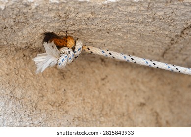 A close up shot of a white patterned nylon rope with a secure knot anchored inside a small hole of a rough textured beige concrete wall
