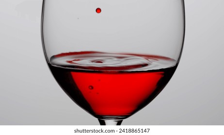 Close up shot of wine glass isolated on white background in studio. Goblet filled with ruby wine, droplets of wine falling inside creating ripples and waves. - Powered by Shutterstock