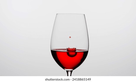 Close up shot of wine glass isolated on white background in studio. Goblet filled with red wine, droplets of wine falling inside creating ripples and crown. - Powered by Shutterstock