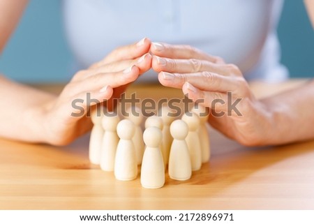 Close up shot of a woman hand guarded protect wooden people on table. Human resources, insurance, human health concepts 
