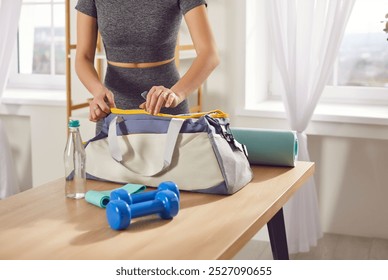 Close up shot of a woman hands packing a sports bag with gym equipment on a table at home. She is preparing for a training session or yoga workout, ensuring all fitness essentials are ready. - Powered by Shutterstock