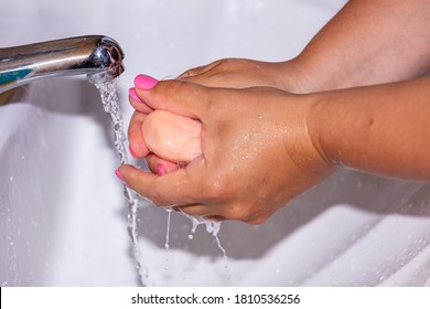 Close Up Shot Of A Woman Lathering Her Hands With A Soap Bar Using Tap Water. Pink Finger Nails. Hygiene Concept.