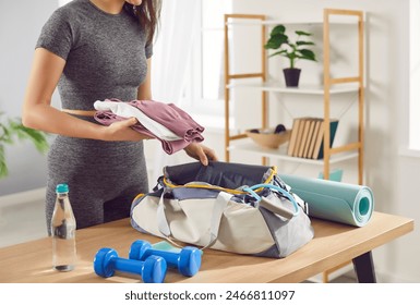 Close up shot of a woman packing a sport bag with equipment and sportswear on table at home. Preparing for a active gym workout, planning fitness and gymnastics or aerobics activities. - Powered by Shutterstock