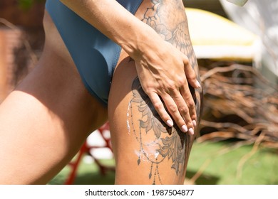 Close shot of woman smears put lotion on her hip, outdoor, sunny day, large tattoo