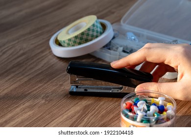Close up shot of a woman touching a stapler with the background of other office equipments on a wooden table