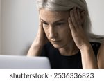 Close up shot worried elderly female worker employee freelancer look on laptop screen rub temples in panic mess confused with bad news in email message. Troubled old lady has serious business problems