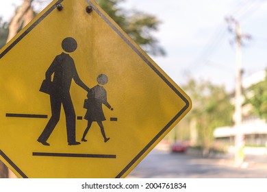 The Close Up Shot Of Yellow Notice Sign Of School And People Crossing The Street At Crosswalk With Beautiful Street Bokeh As A Background During Bright Sunny Day