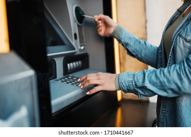 Close up shot of young adult woman using credit card to withdraw money on ATM machine.