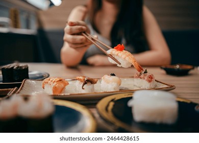 Close up shot of young Asian woman eating fresh nigiri sushi with chopsticks, served with miso soup and salad on the side in a traditional Japanese restaurant. Asian cuisine and food concept. - Powered by Shutterstock