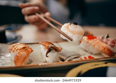 Close up shot of young Asian woman eating fresh nigiri sushi with chopsticks, served with miso soup and salad on the side in a traditional Japanese restaurant. Asian cuisine and food concept. - Powered by Shutterstock