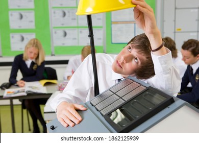 A Close Up Shot Of A Young Boy Adjusting Lamp On A Model House With Solar Panel In A Science Class.