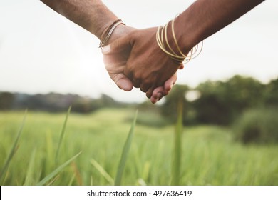 Close Up Shot Of Young Couple Holding Hands In The Field Outdoors. Man And Woman Hand In Hand On Meadow.