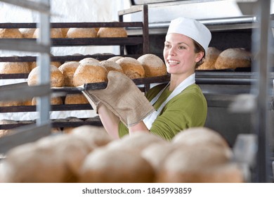 A Close Up Shot Of A Young Female Baker Carrying A Pan Of Fresh Loaves Of Bread Removed From An Oven.