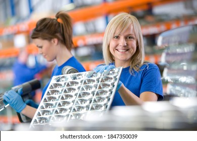 A close up shot of a young female worker smiling and showing aluminum light fittings to the camera.