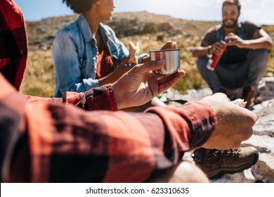 Close Up Shot Of Young Man Relaxing With Friends During A Hike. He Is Eating And Drinking Coffee.