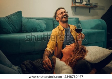 Close up shot of young man sitting down on the floor while his girlfriend lying with head in his lap.Focus on a man with glasses holding a glass of wine and laughing with his eyes closed.Copy space.