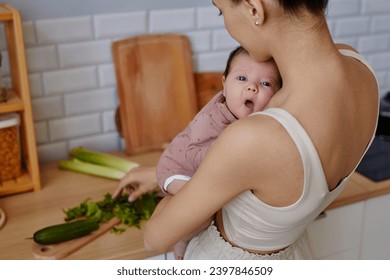 Close up shot of young mother cooking in kitchen and holding cute baby looking at camera - Powered by Shutterstock