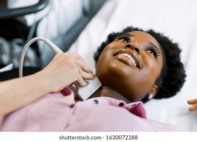 Close Up Shot Of A Young Smiling African American Woman Getting Her Neck And Thyroid Gland Examined By Doctor Using Ultrasound Scanner At The Modern Clinic