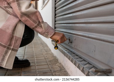 A close up shot  of a young woman lowering the metal fence of her business at the time of closure. Brunette girl crouching to close her sales room once her working day is over
