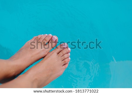 Close show of womans feet with french pedicure gel polish on background of blue water in swimming pool.