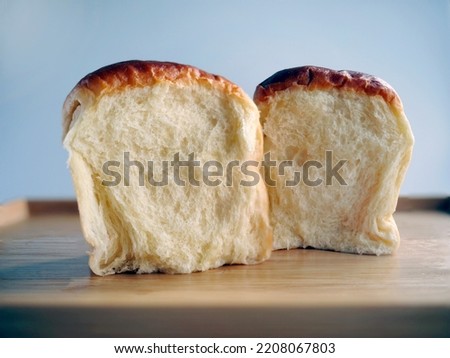 Close up showing the cross section, 2 buns of Fresh baked Japanese Hokkaido soft and fluffy milk bread, Japanese Brioche on the wooden tray with plain background, warm tone