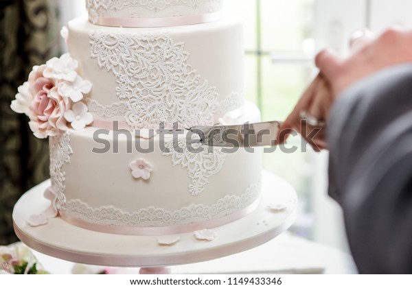 Close up showing a wedding cake being cut.\
Looking along the knife from the couple point of view as the knife\
is just cutting into the cake. The cake is three tiered with pink\
pastel decorations