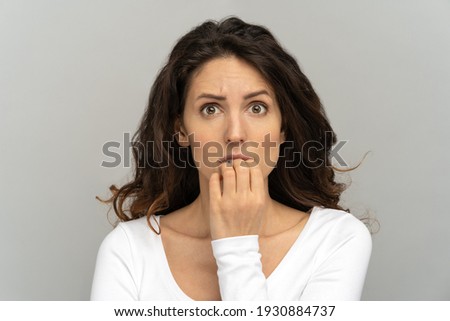 Close up of shy doubtful girl anxious about problem. Studio portrait of awkward young office woman biting nails feeling embarrassed, confused, nervous, looking at camera, isolated on grey background.